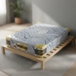 Mattress on a simple wooden bed frame in a sunlit room, wrapped in plastic with a blue-gray patterned cover and corner labels.